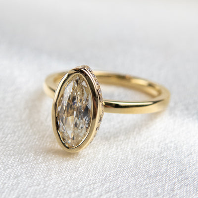 A side view of an elongated marquise-cut diamond ring bezel set with a polished gold band sits elegantly on a soft, white surface.