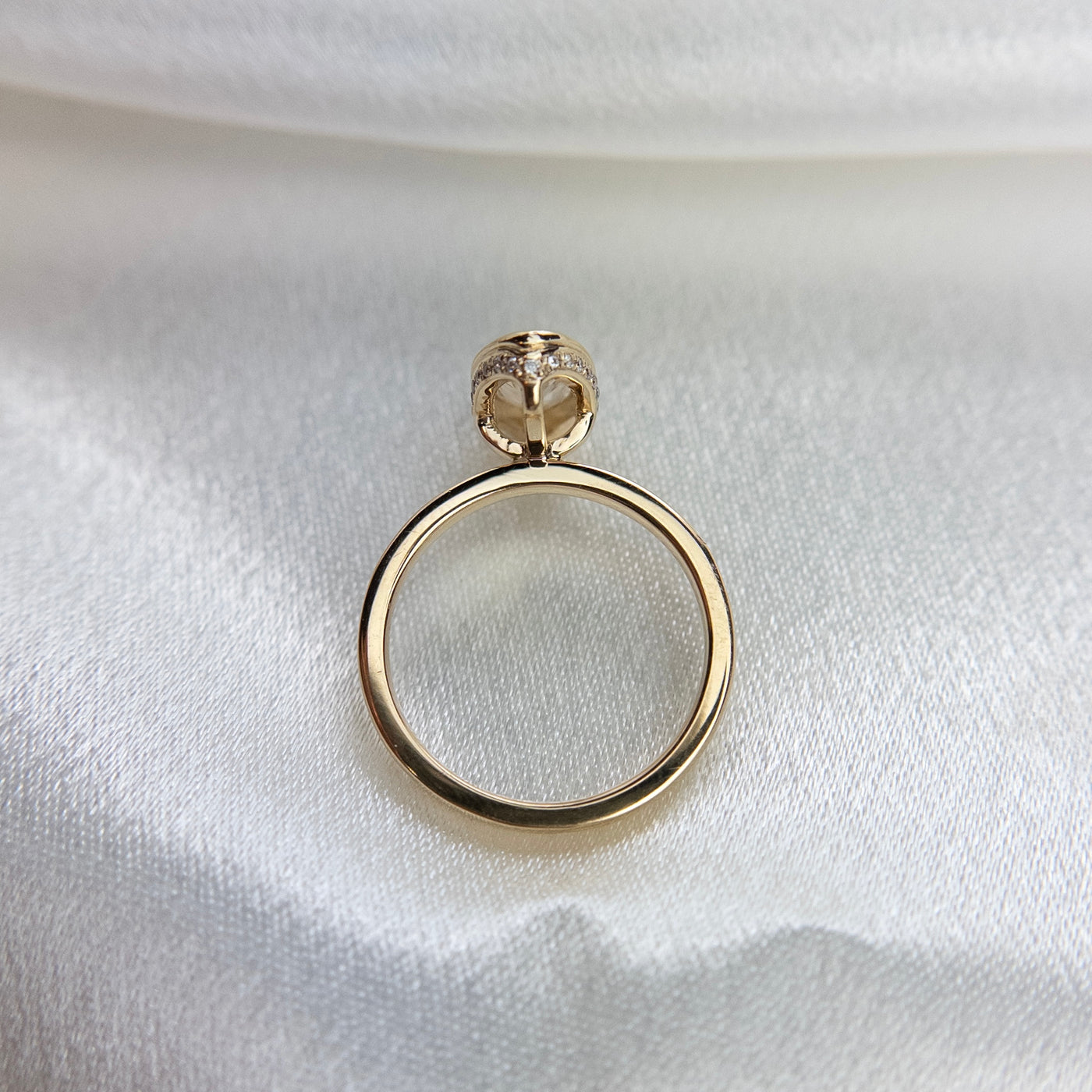 A side profile view of an elongated marquise-cut diamond ring bezel set with a hidden diamond halo and a polished gold band, shown on a white satin surface.