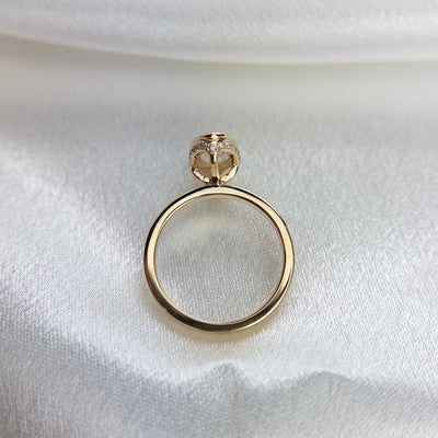 A side profile view of an elongated marquise-cut diamond ring bezel set with a hidden diamond halo and a polished gold band, shown on a white satin surface.