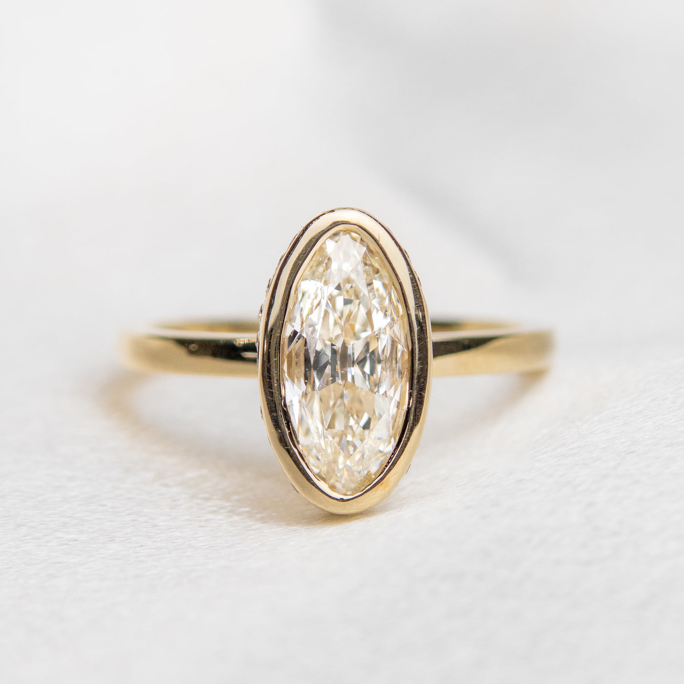 A gold ring with an elongated marquise-cut diamond bezel set with a polished gold band sits elegantly on a soft, white surface.
