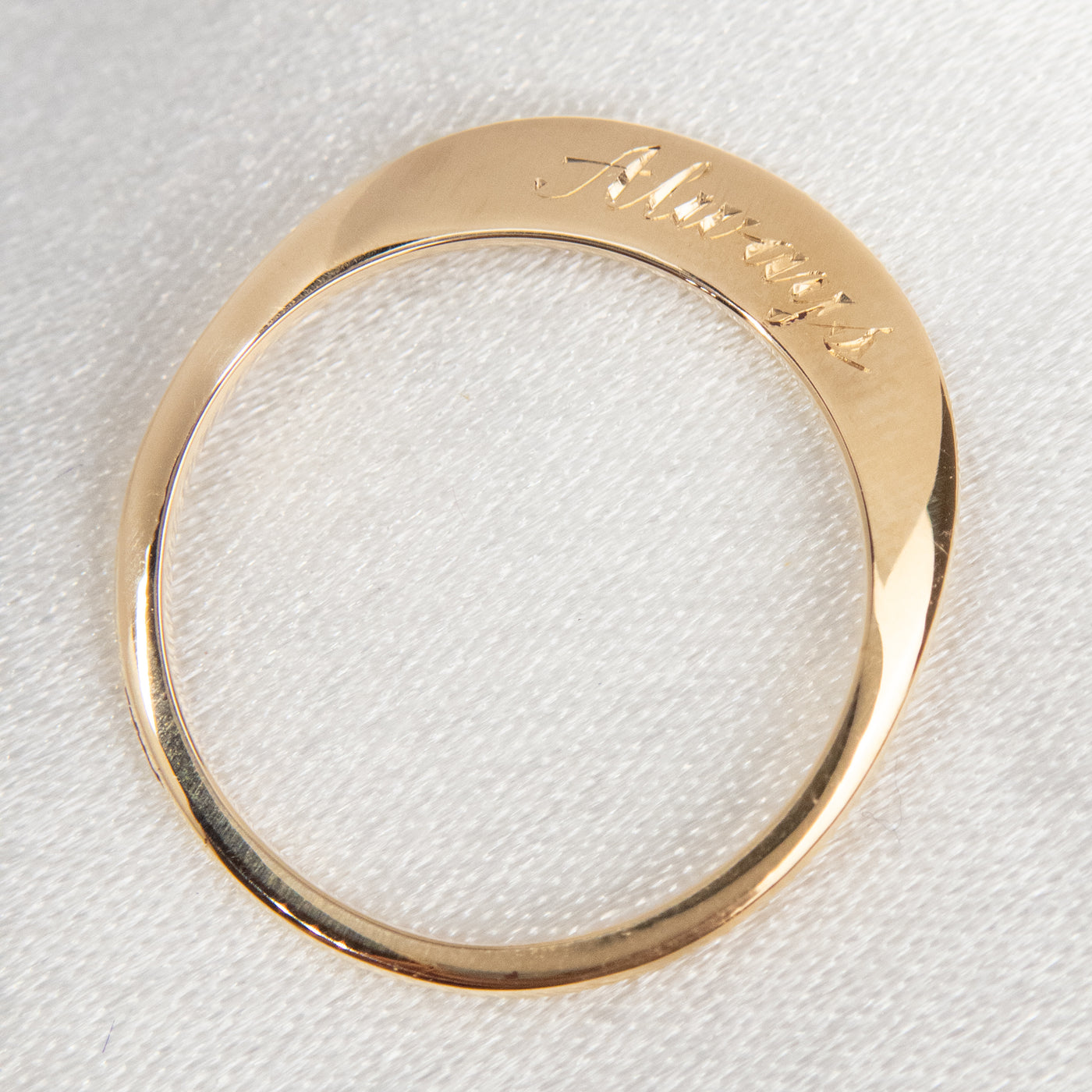 A stunning gold ring with a meaningful quote saying always, shown laying flat on white fabric from above.