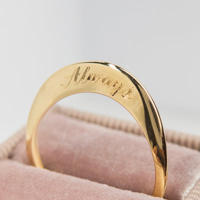 A stunning gold ring with a meaningful quote saying always, shown sitting in a light pink velvet ring box.