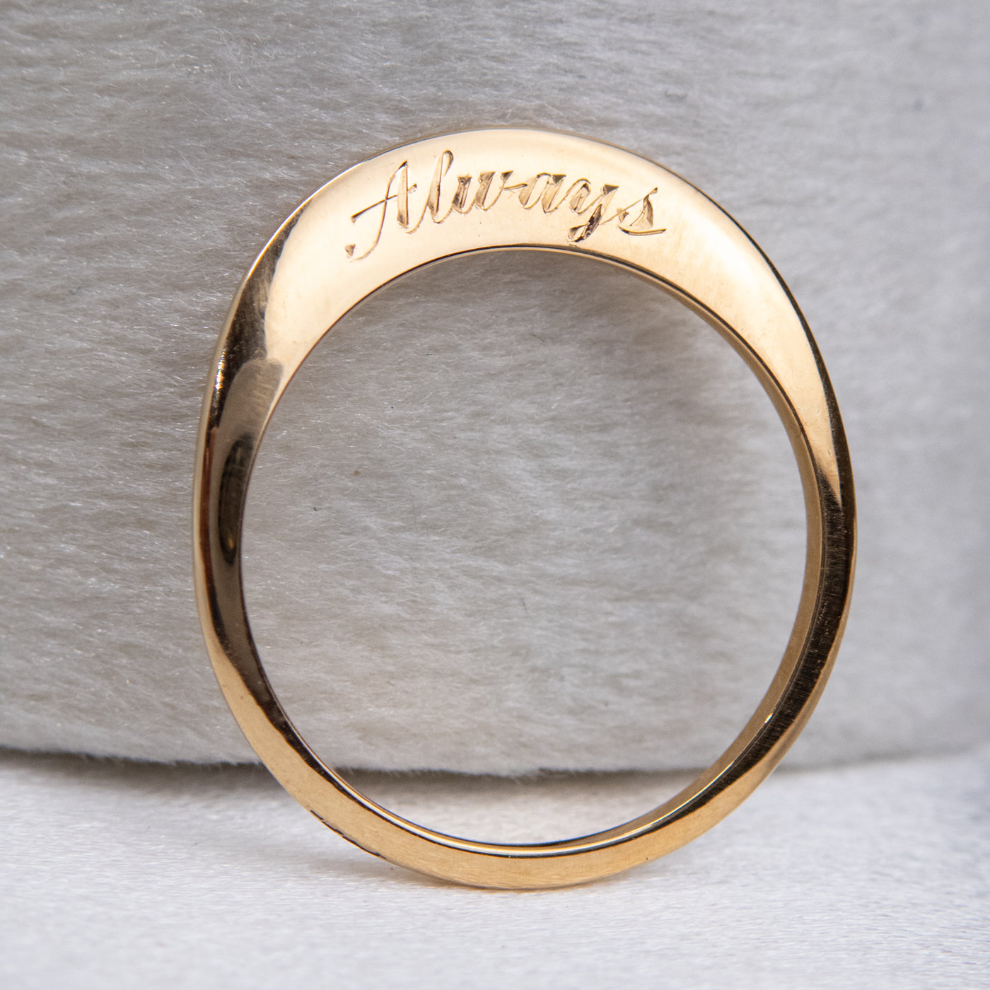 A stunning gold ring with a meaningful quote saying always, shown upright against a velvet ring box.