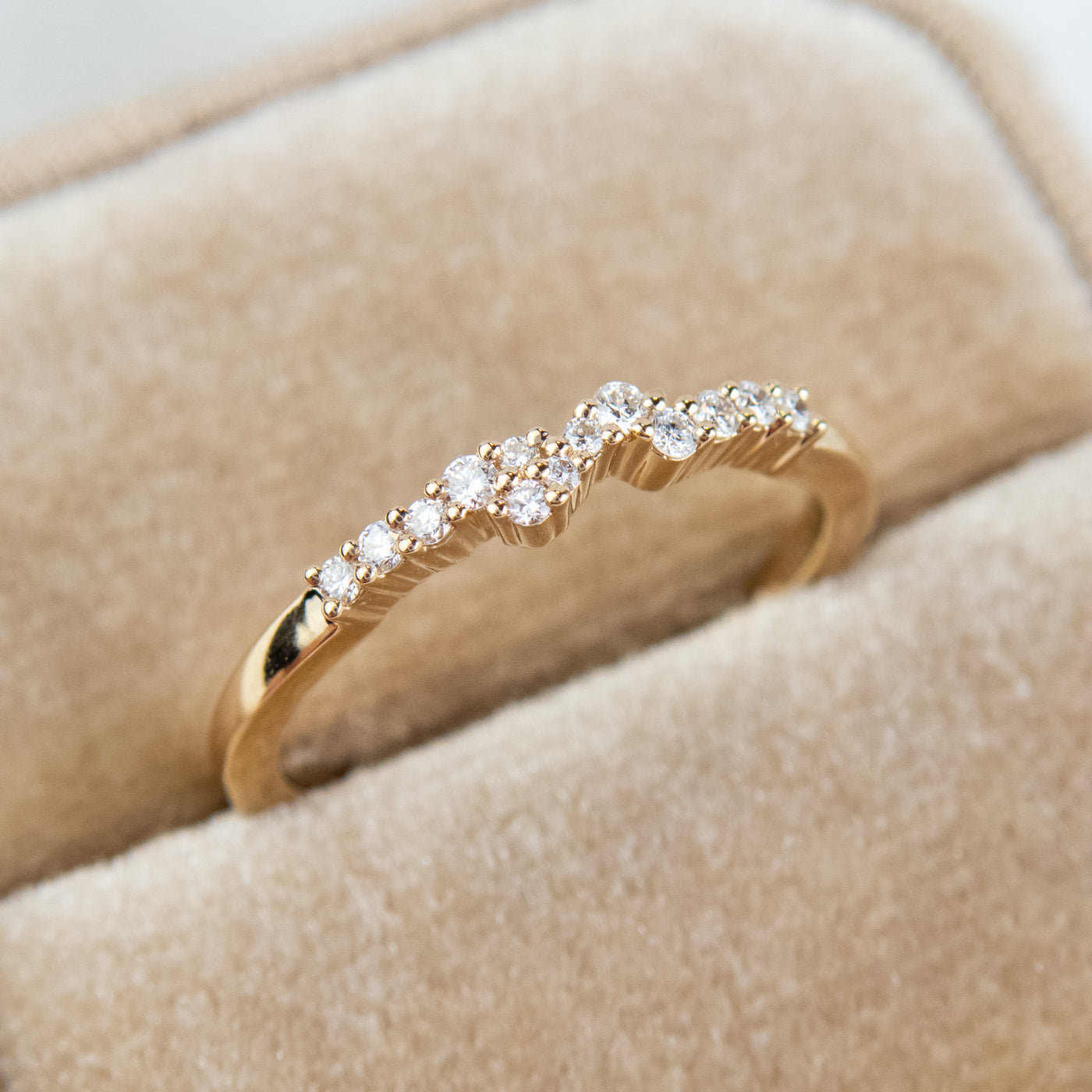 An exquisite gold ring embellished with diamonds, reflecting a timeless elegance and opulence - tucked into a beige velvet jewelry box.