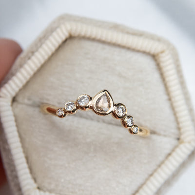 A delicate gold ring with a central pear-shaped diamond, flanked by smaller round diamonds, resting in a soft white ring box.