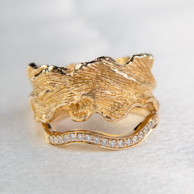An exquisite 14k yellow gold band featuring pave set brilliant diamonds stacked with a gold wide band with natural textures and wavy edges, perfect for adding a touch of luxury to any occasion.
