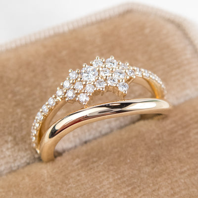 A beautiful gold ring featuring shimmering diamonds and a split band, shown in a beige velvet ring box, perfect as a wedding band or for adding a touch of glamour to any outfit
