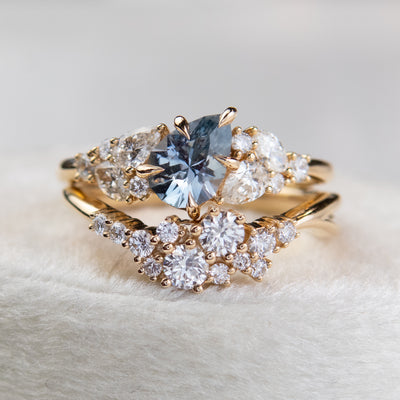 A stunning gold ring featuring a cluster of sparkling diamonds, set in a graduated design stacked with a blue pear shaped sapphire cluster ring. 
