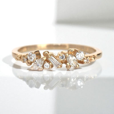 Yellow Gold ring with diamonds clustered across the band in various shapes like round, marquise and baguette on a white background.