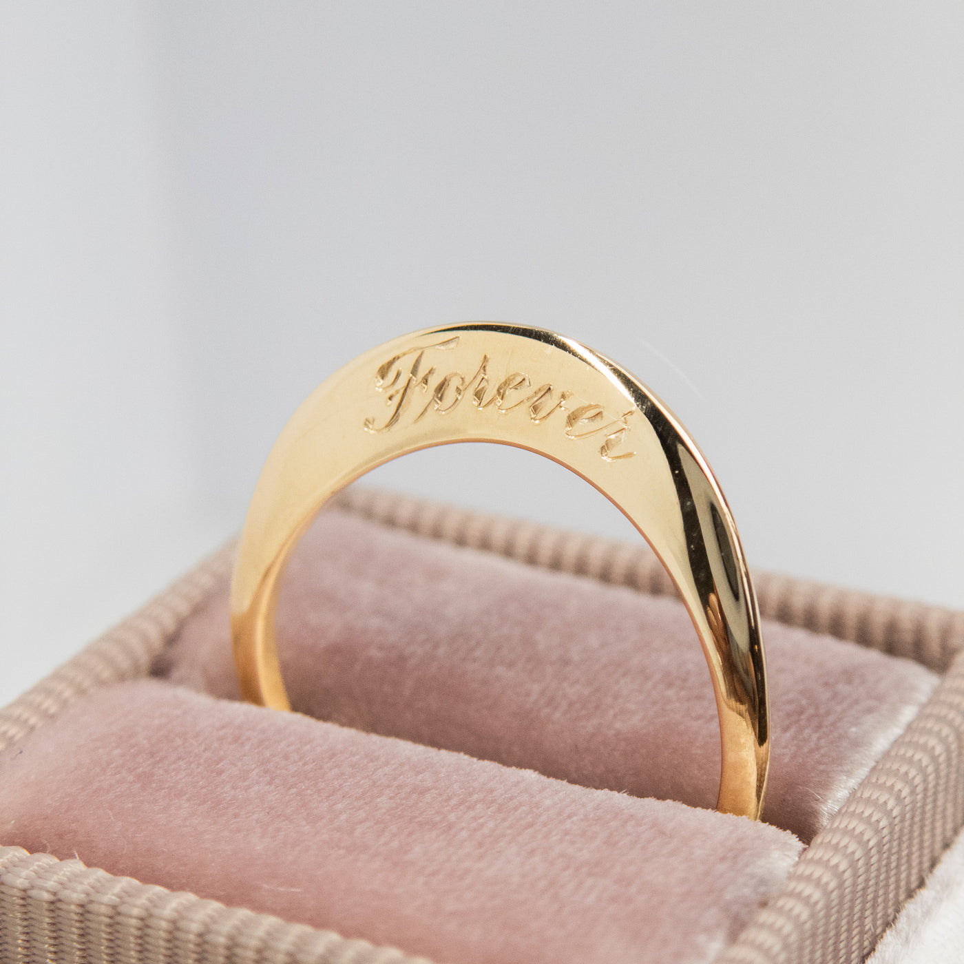A stunning gold ring with a meaningful quote saying love you always, shown nestled in a light pink velvet ring box.