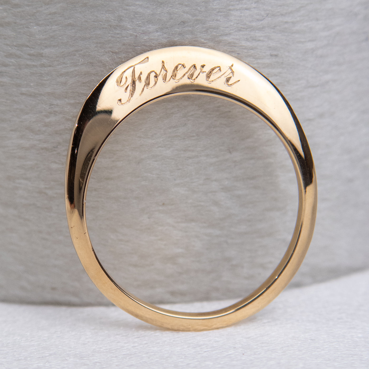 A stunning gold ring with a meaningful quote saying forever, shown upright against a velvet ring box.