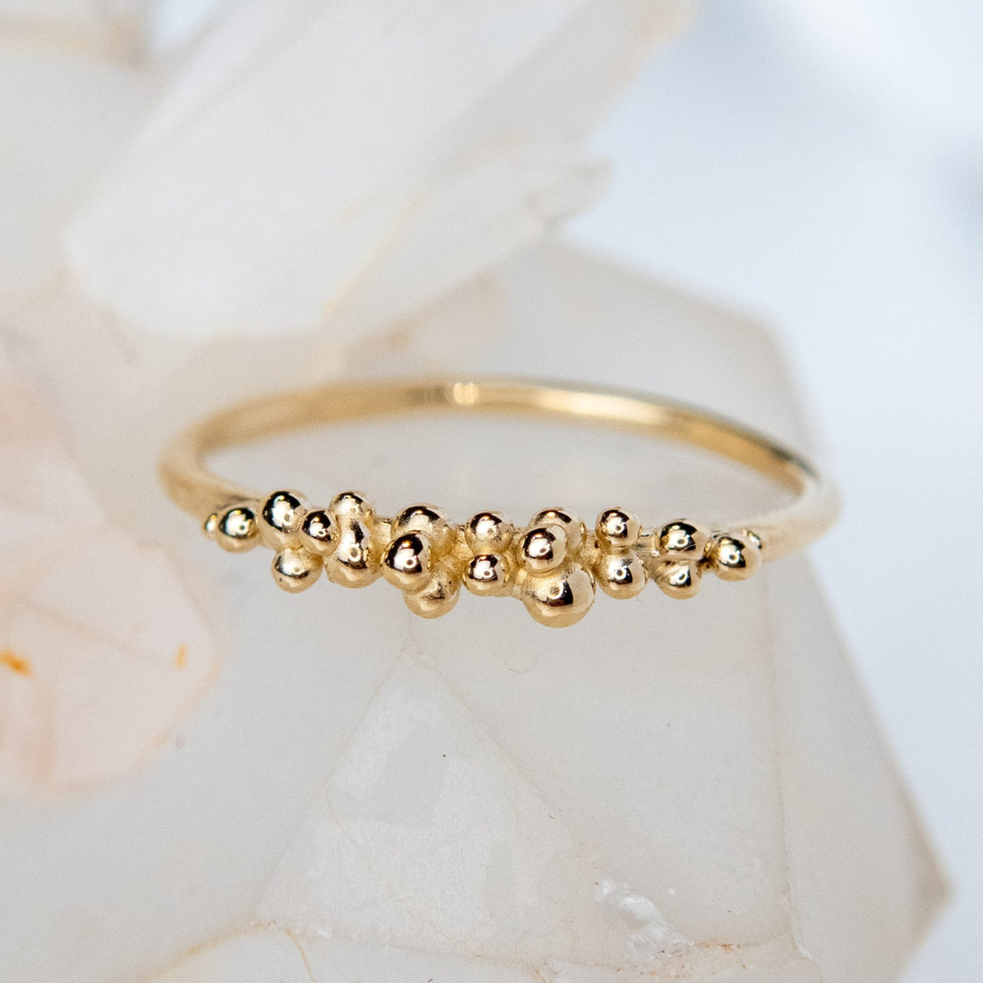 A delicate gold ring adorned with textured, spherical accents, resting on a backdrop of shimmering crystal.