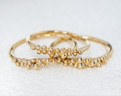 Three yellow gold stacking rings shown together laying on a white surface, each with organically placed gold bubbles.
