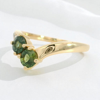 Yellow gold ring with green sapphires and diamond accents on a contour band, on a white background.