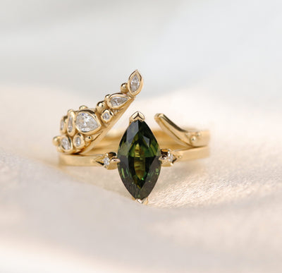 A delicate open gold ring featuring sparkling marquise, pear and round-cut diamonds set in an organic design, stacked with a dark green marquise solitaire engagement ring.