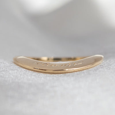 A stunning gold ring with a meaningful quote lying flat to show the profile on white fabric.