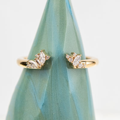 Gold open-ended ring with marquise and round cut diamonds on each end, set on a teal colored ring stand.