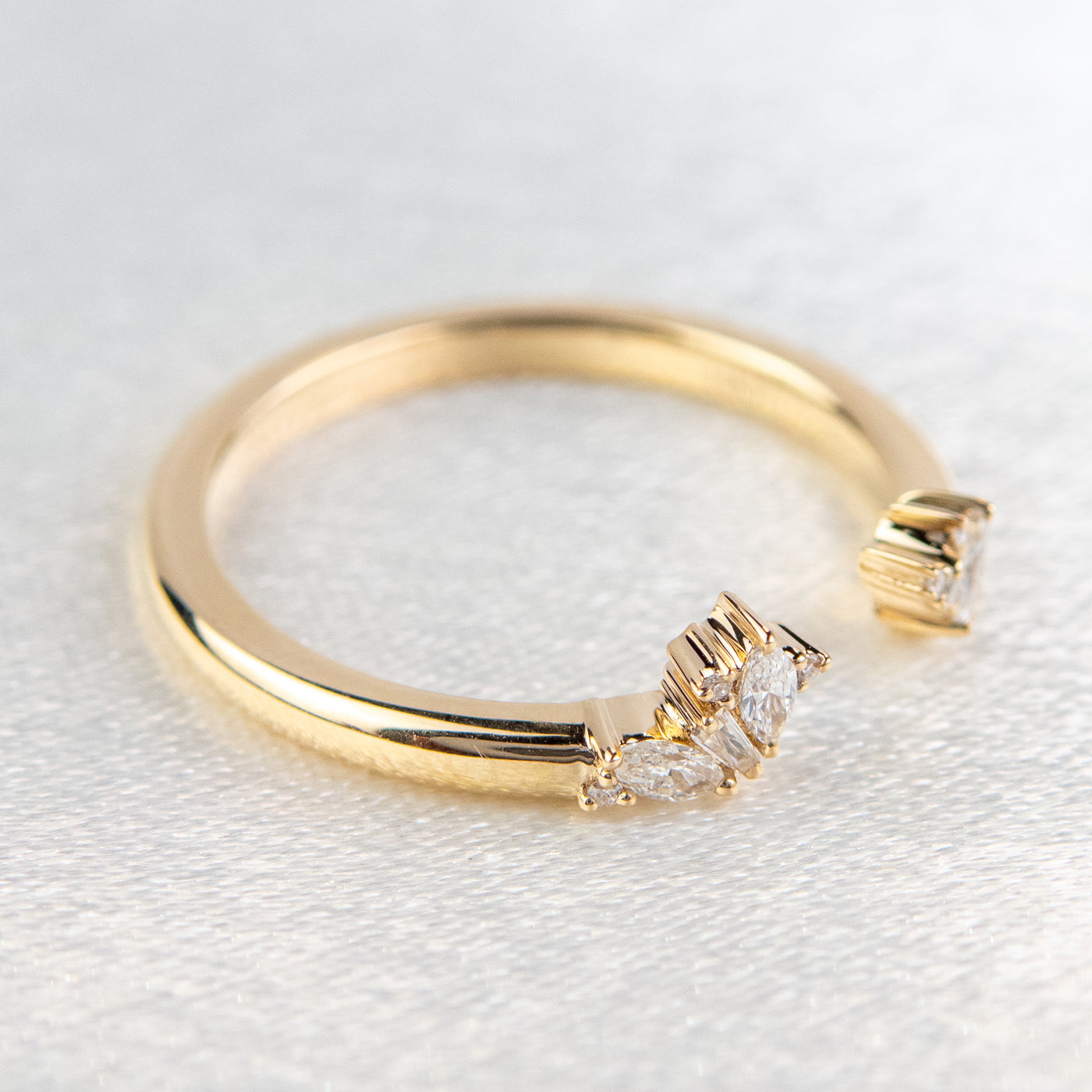 Side view of gold open-ended ring with marquise and round cut diamonds on each end, set on a soft-focus light background.