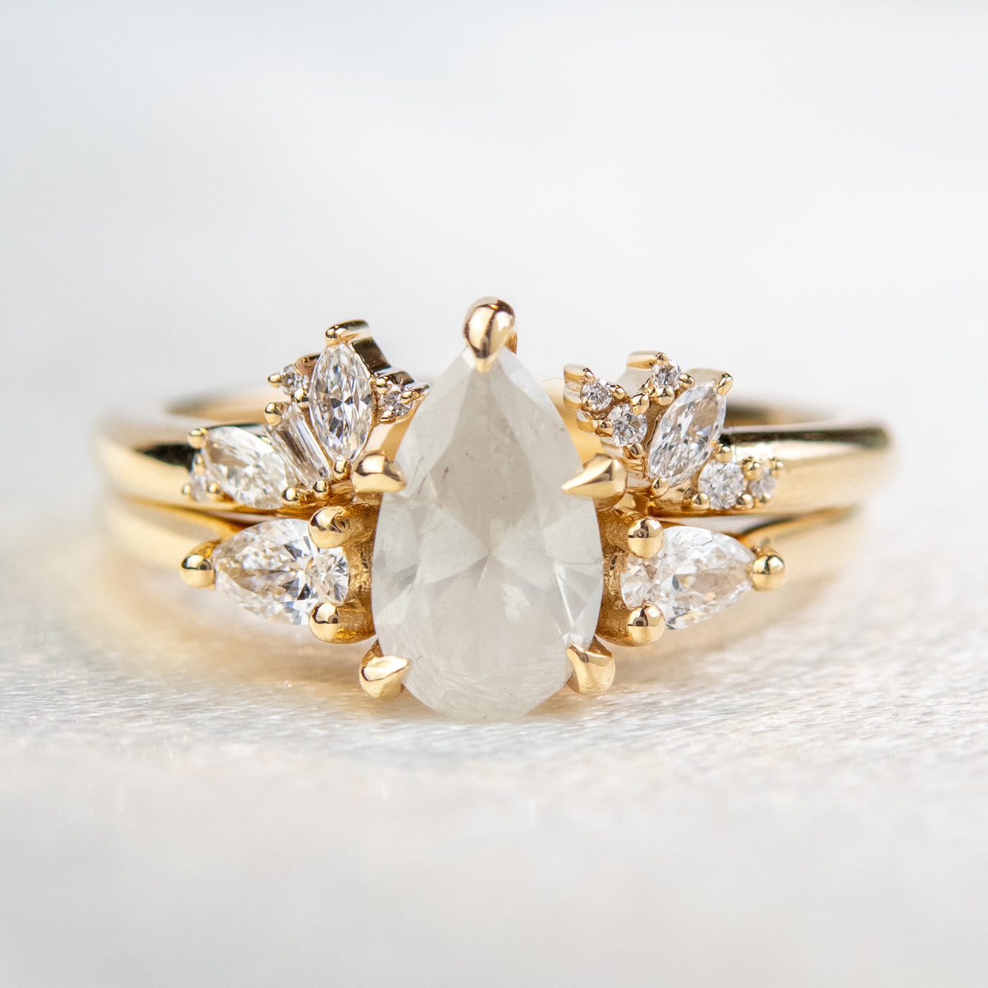 Gold open-ended ring with marquise and round cut diamonds on each end, stacked with an engagement ring on a soft-focus light background.
