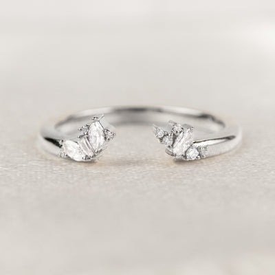 White gold open-ended ring with marquise and round cut diamonds on each end, stacked with an engagement ring on a soft-focus light background.