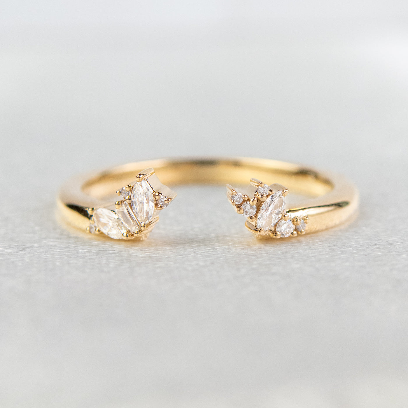 Gold open-ended ring with marquise and round cut diamonds on each end, set on a soft-focus light background.