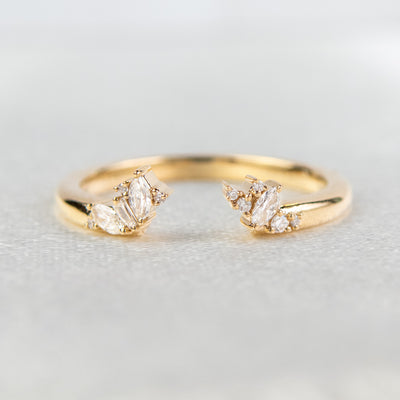 Gold open-ended ring with marquise and round cut diamonds on each end, set on a soft-focus light background.