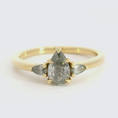 A gold three-stone ring with a fancy grey pear-shaped diamond center and two smaller grey pear-shaped side diamonds.