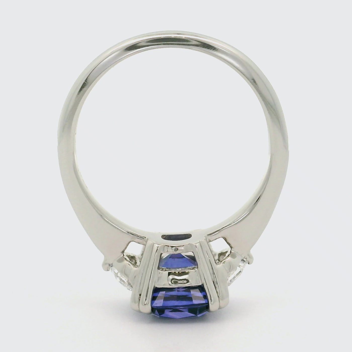 A 360 degree video of a large cushion shaped blue sapphire ring flanked by white cadillac cut diamonds set in a classic platinum setting, shown on a reflective white background. 
