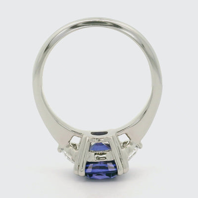 A 360 degree video of a large cushion shaped blue sapphire ring flanked by white cadillac cut diamonds set in a classic platinum setting, shown on a reflective white background. 