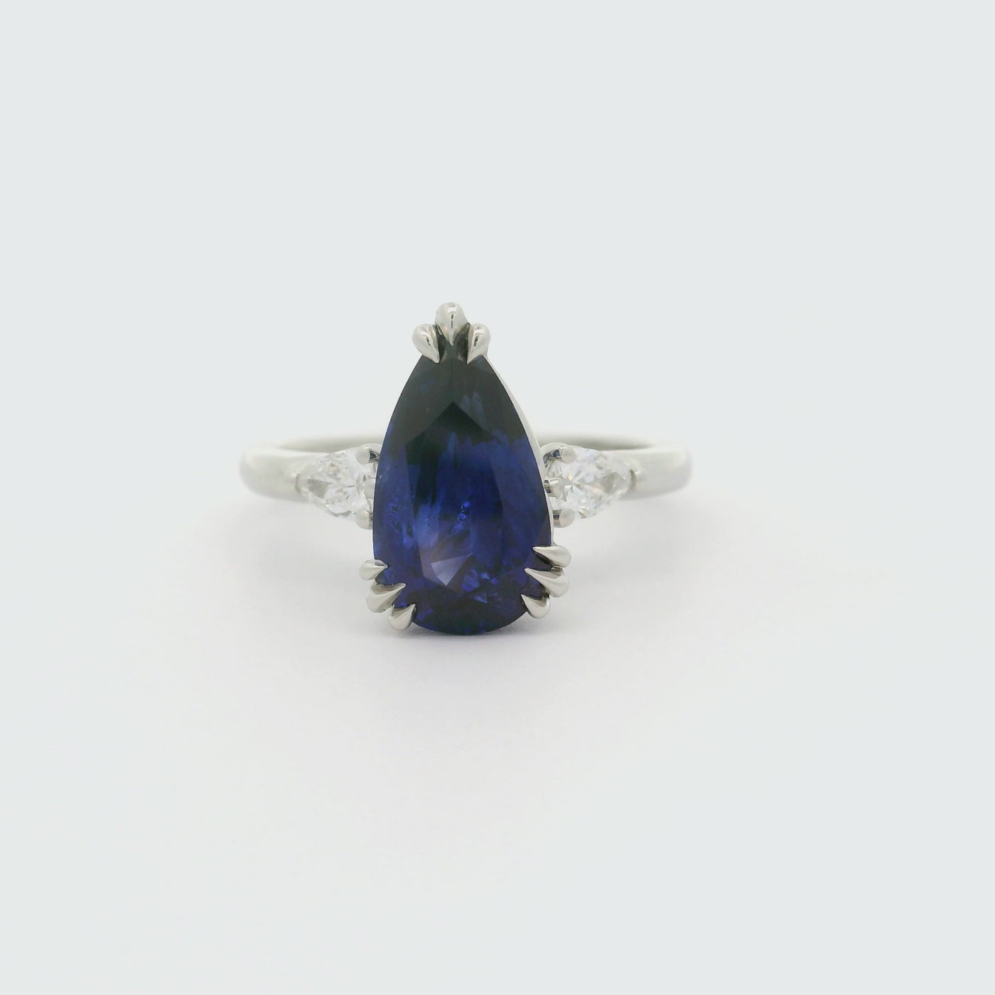 A 180 degree video of a pear-shaped blue sapphire ring with white pear shaped diamond side stones, set in a platinum band. 