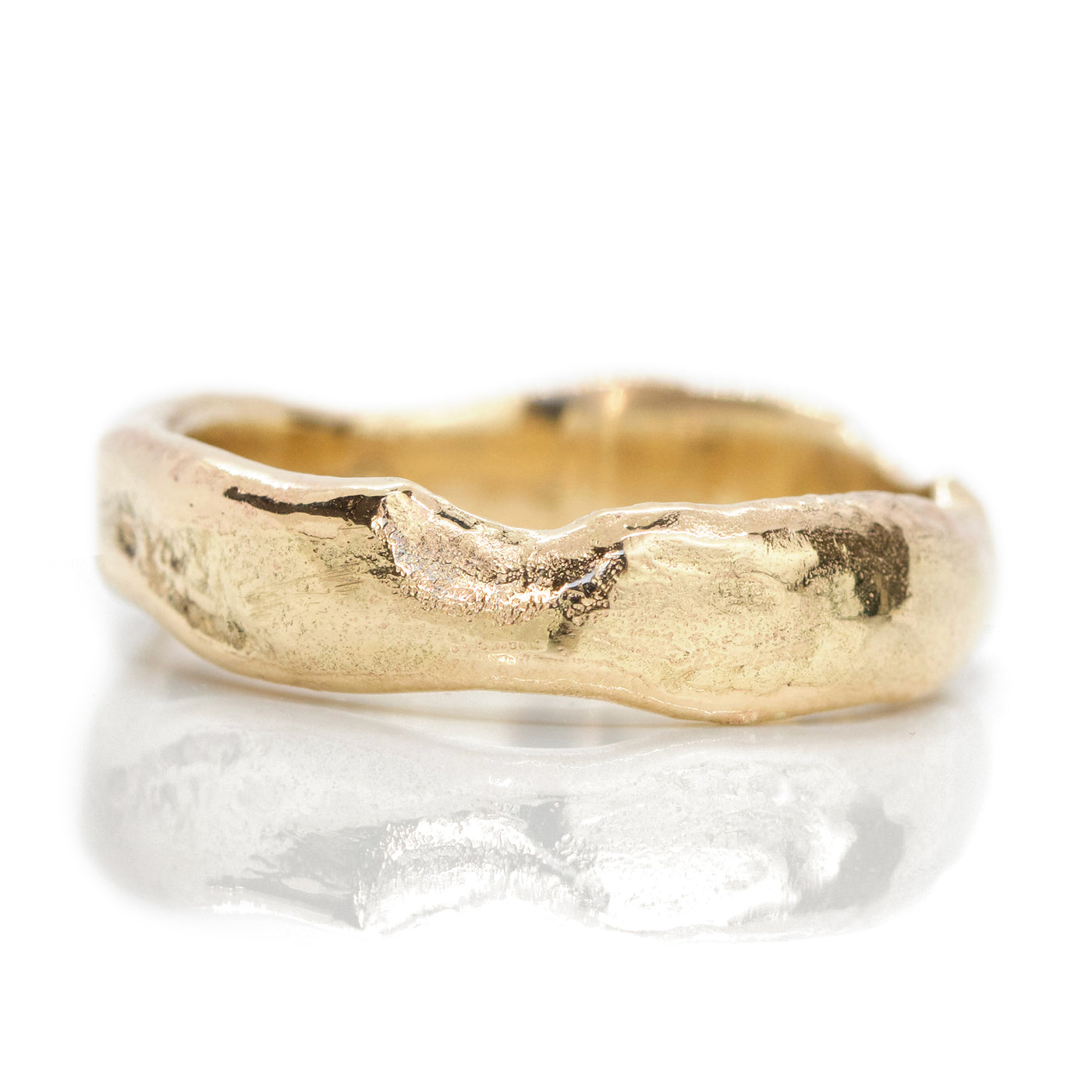 Close-up of a textured gold ring with an organic, uneven edge, reflecting light on a smooth surface.