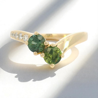 Yellow gold ring with green sapphires and diamond accents on a contour band, on a white background.