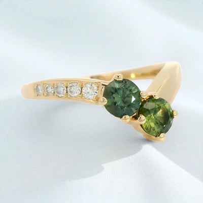 Yellow gold ring with green sapphires and diamond accents on a contour band, on a white background.background