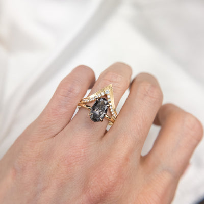 Elegant gold ring with a V-shaped design, encrusted with sparkling diamonds along the band stacked on a finger with a salt and pepper diamond solitaire engagement ring.