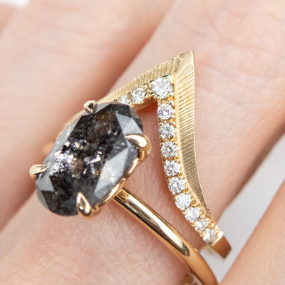 Elegant gold ring with a V-shaped design, encrusted with sparkling diamonds along the band stacked on a finger with a salt and pepper diamond solitaire engagement ring.