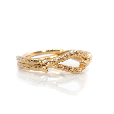 A gold ring handcarved to resemble the branches of a tree, the branches form the band and are twisted to form a beautiful ring, lying on a white surface.