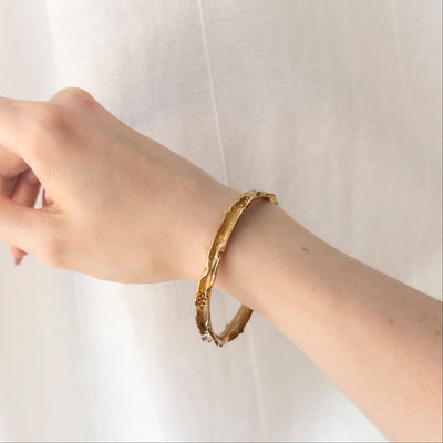 Gold bracelet on a wrist against a white background