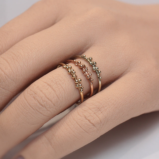 Rings in various metals including yellow gold, white gold and rose gold stacked on a finger featuring gold bubble details.