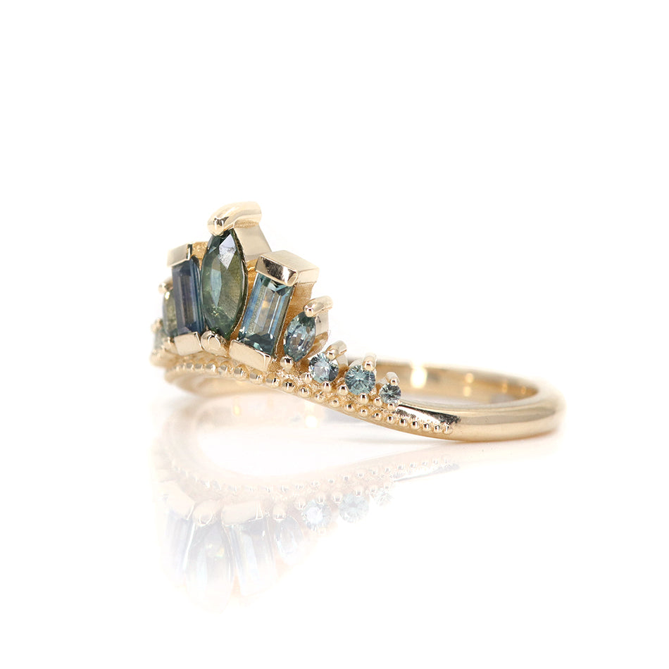 A delicate gold ring adorned with blue and teal sapphires, featuring a central marquise stone and two rectangular stones, reflecting light beautifully shown from the side.