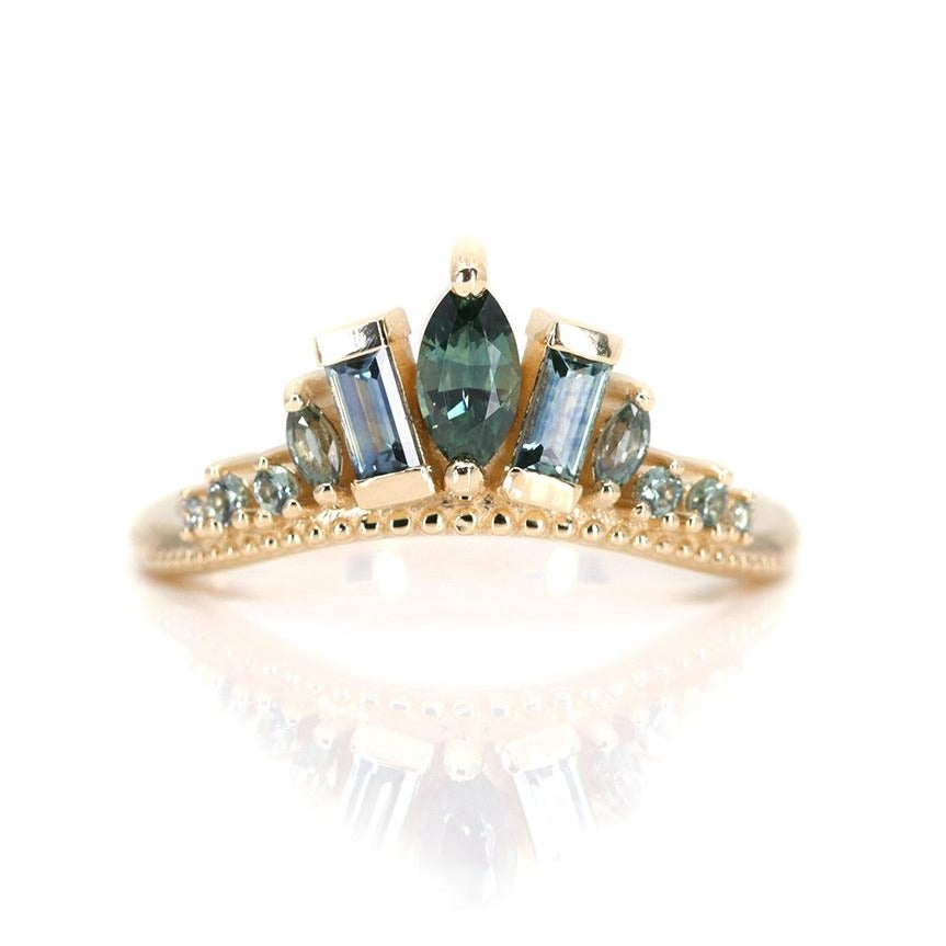 A delicate gold ring adorned with blue and teal sapphires, featuring a central marquise stone and two rectangular stones, reflecting light beautifully.