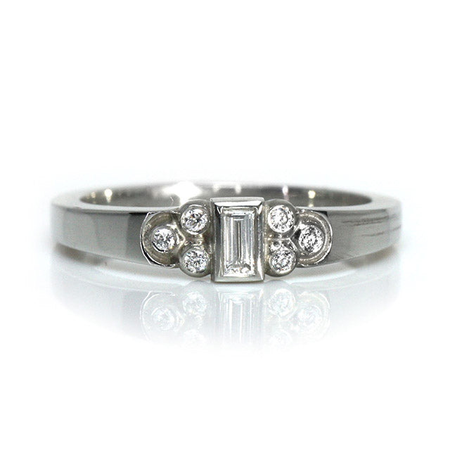 Elegant white gold ring with a central rectangular-cut diamond flanked by six small round diamonds, shown on a white background. 