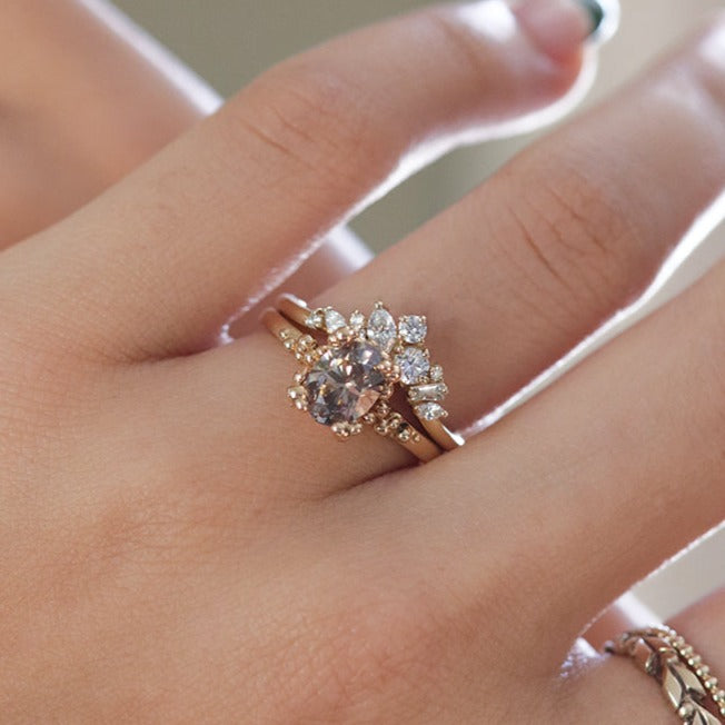 A delicate 14kt gold ring featuring a cluster of sparkling diamonds in various shapes, elegantly stacked on a finger with an oval salt and pepper diamond engagement ring.