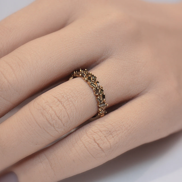 Gold ring featuring an intricate pattern of alternating champagne baguette diamonds and decorative bead accents shown on a finger.