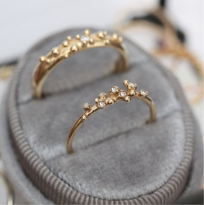 Two elegant gold rings adorned with sparkling gems, displayed on a soft grey velvet jewelry box.
