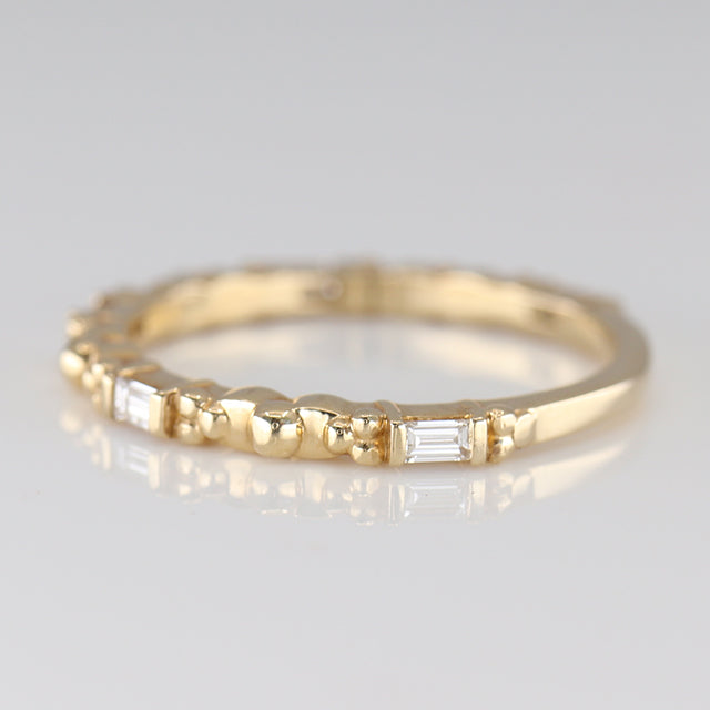 A delicate gold ring featuring alternating round and baguette-shaped stones, reflecting light with elegant simplicity shown from the side.