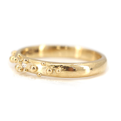 Gold ring with small bubble textures and a central diamond, reflecting a unique and contemporary design shown from the side.