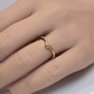 A delicate yellow gold ring featuring a curved design adorned with shimmering diamonds along one side and organically placed gold bubbles on the other shown on a finger.