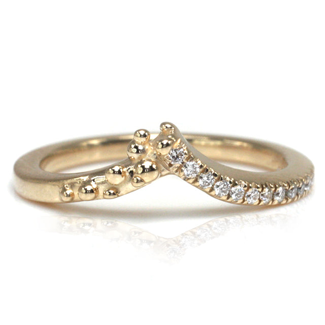 A delicate yellow gold ring featuring a curved design adorned with shimmering diamonds along one side and organically placed gold bubbles on the other.