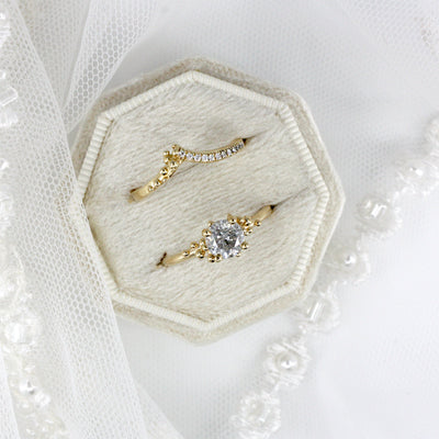 Two elegant gold rings displayed on a soft, octagonal ring box, surrounded by delicate lace and beaded embellishments.