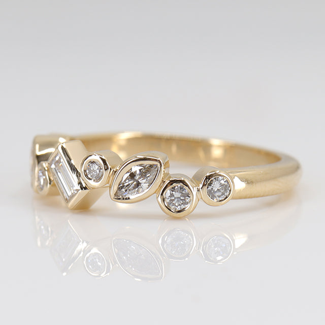 A stylish gold ring featuring assorted diamond shapes, including marquise, round emerald cut, set in a delicate bezel alternating design shown from the side.